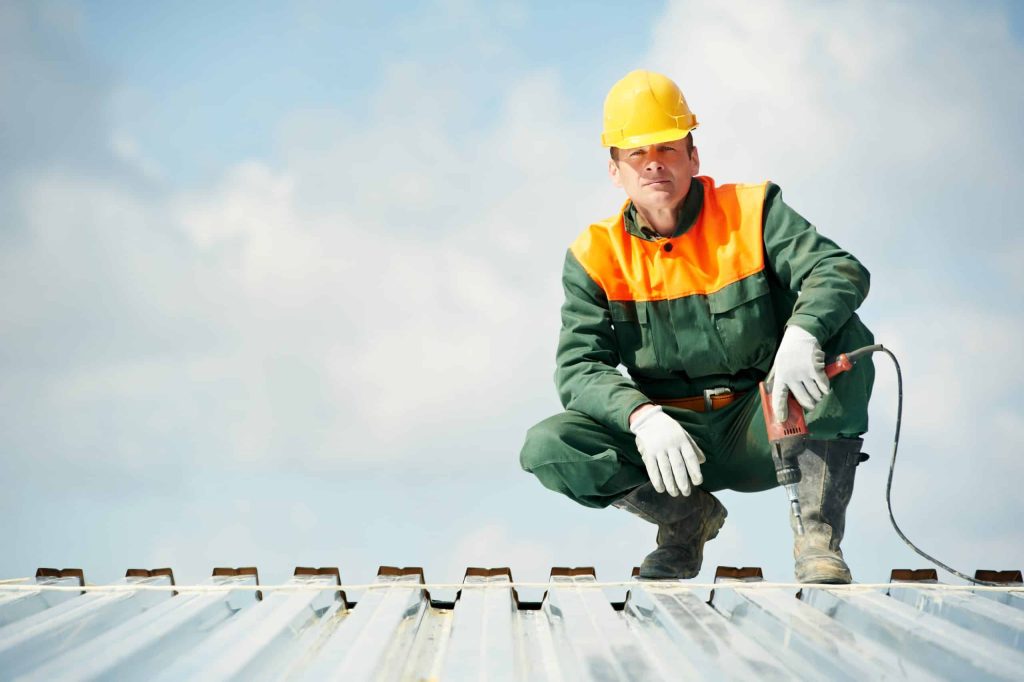 roofer with a hand drill on top of a metal roof